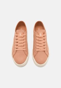 Broskvové plátěné tenisky s texturovaným povrchem, kulatými tkaničkami, bílou gumovou podrážkou a vyraženým logem na jazyku.