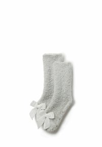 Miękkie szare futrzane skarpetki z białymi satynowymi kokardkami i małymi punktami antypoślizgowymi na podeszwach, leżące płasko na białym tle.
