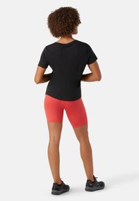 Černé tričko s krátkým rukávem, červené přiléhavé šortky a černé sportovní boty. Oblečení má jednoduchý design a hladkou texturu.
