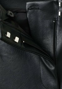 Veste en cuir noir avec une finition texturée, dotée de poches zippées et d'accents en métal sur le devant et les bords.