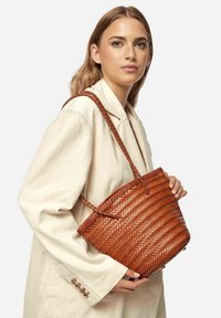 Borsa a mano in pelle marrone intrecciata con una parte superiore arrotondata, doppi manici intrecciati e un motivo a chevron testurizzato. Mostra un design liscio e robusto.
