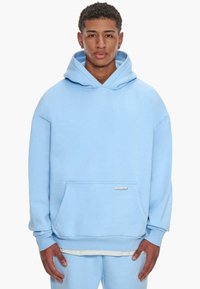 Light blue hooded sweatshirt made of soft fabric, featuring a front pocket and ribbed cuffs. Simple design without patterns or accents.