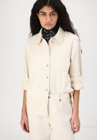 Cream-colored button-up shirt made of soft material, featuring two front pockets and rolled sleeves, paired with matching pants.