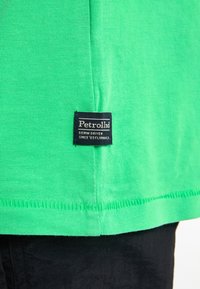 Groen katoenen T-shirt met een textuurafwerking, met een zwart logo-label genaaid aan de onderzijde en contrasterende stiksels langs de zoom.