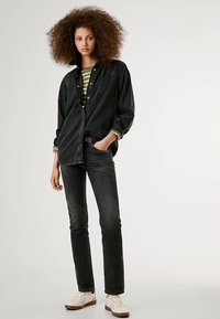 Camisa de ganga preta sobreposta a uma blusa às riscas verdes e brancas, combinada com jeans escuros e sapatilhas brancas. Ajuste casual e texturizado.