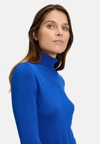 Blauer Rollkragenpullover mit figurbetontem Design, gerippter Textur und langen Ärmeln, aus weichem Strickmaterial gefertigt.