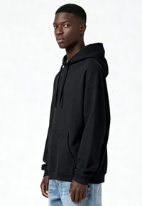 Fekete kapucnis pulóver elülső zsebbel, bordázott mandzsettákkal és laza szabással. A kapucnin húzózsinór található. Világoskék farmerrel viselve.