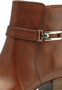 Bottines en cuir brun avec un design cintré, une accent en boucle métallique et une finition texturée. Présente un talon bloc et une couture contrastée.