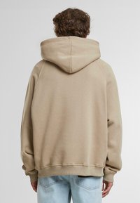 Felpa con cappuccio color beige chiaro, realizzata in tessuto morbido. Presenta una vestibilità rilassata, polsini a coste e una tasca a marsupio sul davanti.