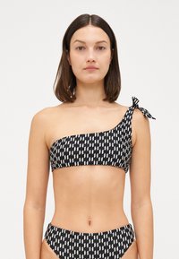 Bikini v črno-beli vzorčasti zasnovi z zgornjim delom na eno ramo, ki ima vezno podrobnost. Gladko blago, geometrijski vzorec, ujemajoči se visokoodpasni spodnji del.