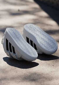 Bijele cipele s crnim trostrukim prugama, imaju teksturiranu gumenastu potplatu i glatki gornji dio za svakodnevno nošenje.