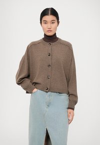 Hnedý pletený kardigán s rebrovanou textúrou, veľkými gombíkmi a voľným strihom, skombinovaný s svetlomodrou džínsovou sukňou s predným rozparkom.