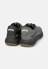 Grijze en zwarte sneakers met "CAMPER" branding op de hiel, featuring een gestructureerde zool en reflecterende accenten op de bovenkant.
