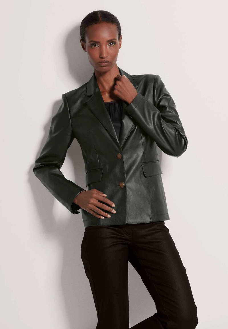 Donkergroene leren blazer met een getailleerde pasvorm, reverskraag, twee voorzakken en twee knopen. Gecombineerd met zwarte slim-fit broek.