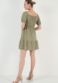 Green, knee-length dress with a textured fabric, short puff sleeves, a fitted waist, and a ruffled hem. Paired with beige high heels.