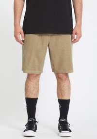 Bomuldsshorts i khaki farve med en afslappet pasform, der har lommer og en struktureret overflade, parret med sorte høje sokker og sneakers.