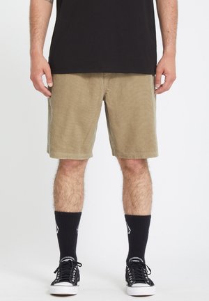 Kordshorts in Khakifarbe mit entspannter Passform, ausgestattet mit Taschen und einer strukturierten Oberfläche, kombiniert mit schwarzen hohen Socken und Sneakers.