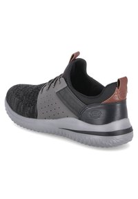 Zapatillas deportivas para hombre en material de punto negro y gris con detalles perforados, suela de goma resistente y acento marrón en el talón.