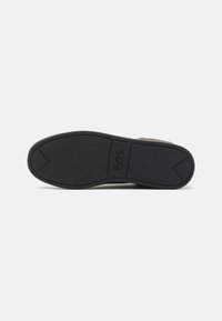 Semelle de chaussure en caoutchouc noir avec une surface texturée, dotée d'un bout arrondi et d'un logo de marque en relief bien visible sur le côté.