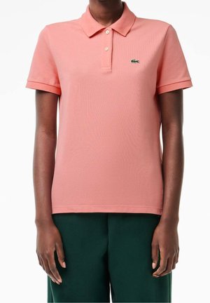 Różowa bawełniana koszulka polo o teksturowanym wykończeniu, z klasycznym kołnierzykiem, krótkimi rękawami i małym zielonym logo po lewej stronie klatki piersiowej.