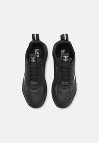 Baskets de sport noires avec une tige synthétique texturée, fermeture à lacets, bout renforcé et accents argentés contrastants sur le côté et le talon.