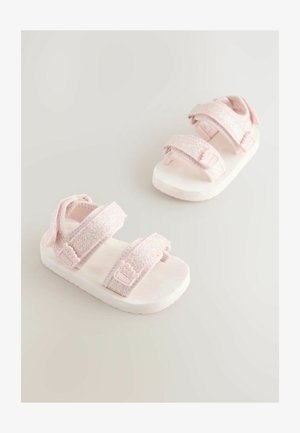 Sandalias rosas con tiras brillantes, con dos cierres ajustables de velcro y una suela suave. Acentuadas con un diseño floral en la correa.