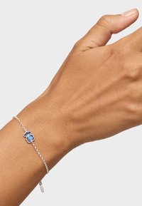 Bracciale in argento con un ciondolo a forma di orso blu con una finitura lucida. Il bracciale è indossato su un polso con una texture della pelle visibile.