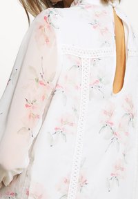 Floral blouse in lightweight, white fabric with pink and green prints. Features a keyhole back and lace accents along the seams.