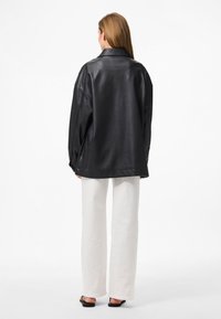 Schwarze Lederjacke im Oversized-Stil mit Reverskragen, versehen mit abgesenkten Schultern und einer glatten Textur, kombiniert mit weißen weit geschnittenen Hosen.