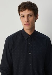 Marineblaues Hemd mit Knöpfen und einem subtilen goldenen Punktmuster, klassischem Kragen und einer einzelnen Brusttasche, gefertigt aus einem glatten Stoff.