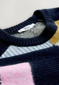 Pull en laine avec col côtelé bleu marine et motif géométrique multicolore en bleu, rose, moutarde et gris, étiquette "NEXT" à l'intérieur du col.