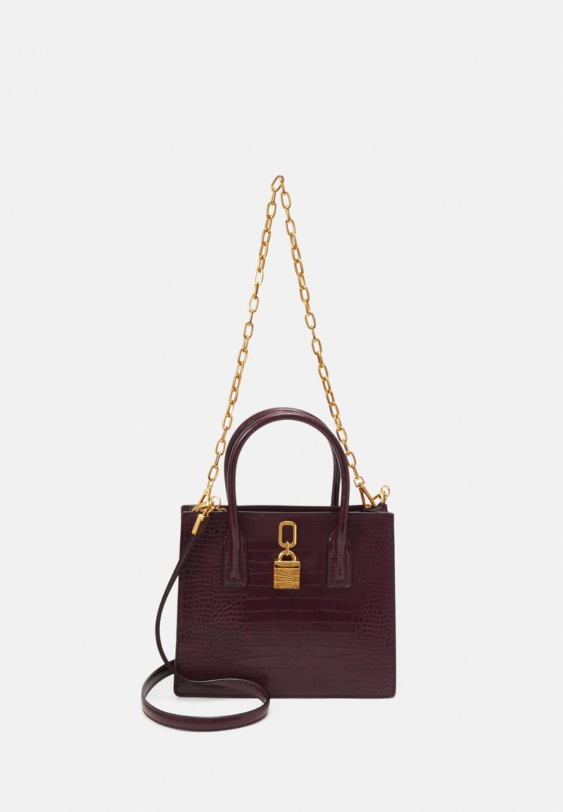 Sac à main bordeaux foncé à texture crocodile avec bandoulière chaîne dorée, poignées supérieures et un cadenas doré à l’avant sur fond uni.