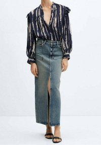 Blusa rigata blu navy e crema con maniche a sbuffo e chiusura a bottoni, abbinata a una gonna di denim a vita alta con spacco frontale e finitura sbiadita.