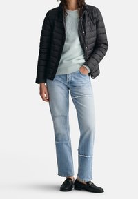 Black quilted jacket, light blue sweatshirt with embossed design, light denim jeans with patchwork details, black loafers.
