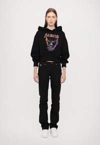 Hoodie cropped nera con stampa grafica, abbinata a jeans neri a vita alta e sneakers bianche. Design semplice e aderente.