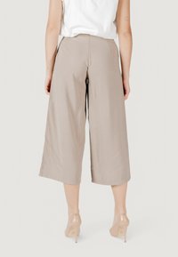 Culottes anchos de color beige, confeccionados con una tela suave, con cintura alta y bolsillos en las costuras laterales. Llevados con tacones altos transparentes.