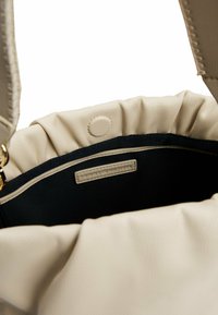 Borsa a tracolla beige con texture, dotata di una parte superiore arricciata e un interno blu navy. Presenta una chiusura a scatto e un'etichetta del marchio all'interno.
