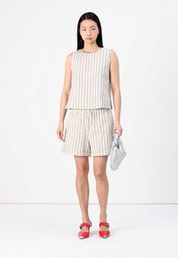 Set iz brezrokavnega zgornjega dela in kratkih hlač iz mešanice lana z navpičnimi črtami v krem in bež barvi. Dodatki vključujejo srebrno torbico in rdeče petke.