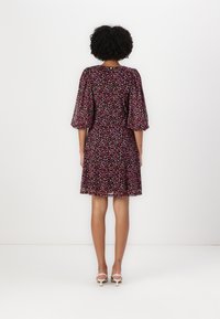 Robe noire avec un motif de pois colorés, des manches bouffantes et une jupe évasée. Assortie avec des sandales à talons hauts blanches.