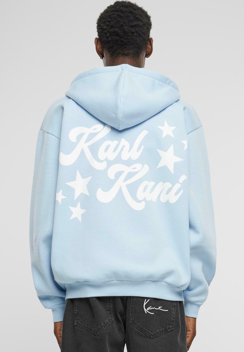 Helle blaue Kapuzenjacke mit weißem "Karl Kani"-Text und Sternen-Grafiken auf der Rückseite; ausgestattet mit einer Kordelzugkapuze und gerippten Bündchen.
