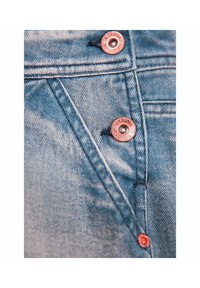 Denim-kangas vaaleansinisessä sävyssä, jossa on haalistunut tekstuuri. Varustettu metallinhohtoisilla punaisilla nappeilla ja näkyvillä ompelusyillä taskujen ja sauman kohdalla.