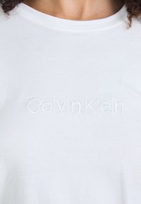 Vit t-shirt med subtil, broderad "Calvin Klein" logotyp på bröstet, som visar en minimalistisk design och klassisk stil.