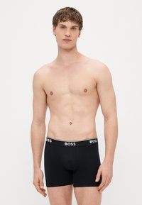 Μαύρα βαμβακερά μποξεράκια με λευκή ελαστική ζώνη μέσης που φέρει το λογότυπο "BOSS". Λεία υφή και εφαρμοστή σχεδίαση, κατάλληλα για καθημερινή χρήση.