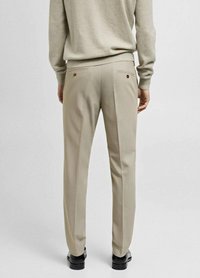 Pantalon beige au talonnage ajusté, doté de deux poches arrière avec fermetures à bouton, et d'un tissu lisse et texturé.