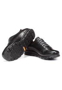 Scarpe in pelle nera con finitura liscia, dotate di lacci elastici grigi e suola in gomma testurizzata con un motivo di battistrada prominente.