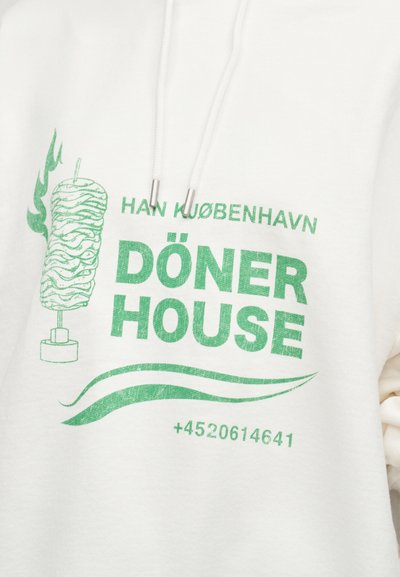 Λευκή μπλούζα με κουκούλα με πράσινο κείμενο "DÖNER HOUSE" και κάθετο γραφικό από σουβλάκι κρέατος, αριθμό τηλεφώνου, και τη φράση "HAN KJØBENHAVN" πάνω από το κείμενο.