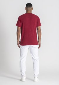 Röd ribbad t-shirt med rund hals och korta ärmar, ihopparad med vita byxor och vita sneakers, sedd bakifrån.