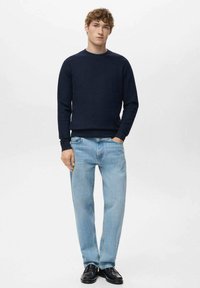 Marineblauer Crewneck-Pullover, kombiniert mit hellblauen Jeans mit lockerem Schnitt und geraden Beinen, ergänzt durch schwarze Schuhe.