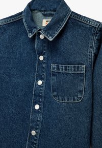 Mørk denimskjorte med knap-trykkrave, der har sølvfarvede knapper og en enkelt brystlomme. Klassisk design med struktureret stofstruktur.