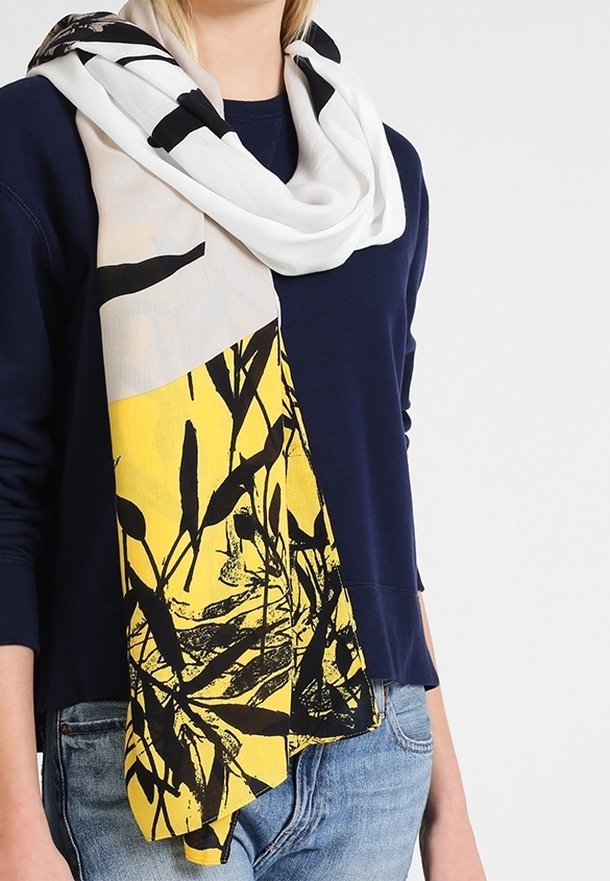 Écharpe légère et tissée en blanc, jaune et noir avec un imprimé botanique ; se drape en boucle autour du cou, avec une texture douce.